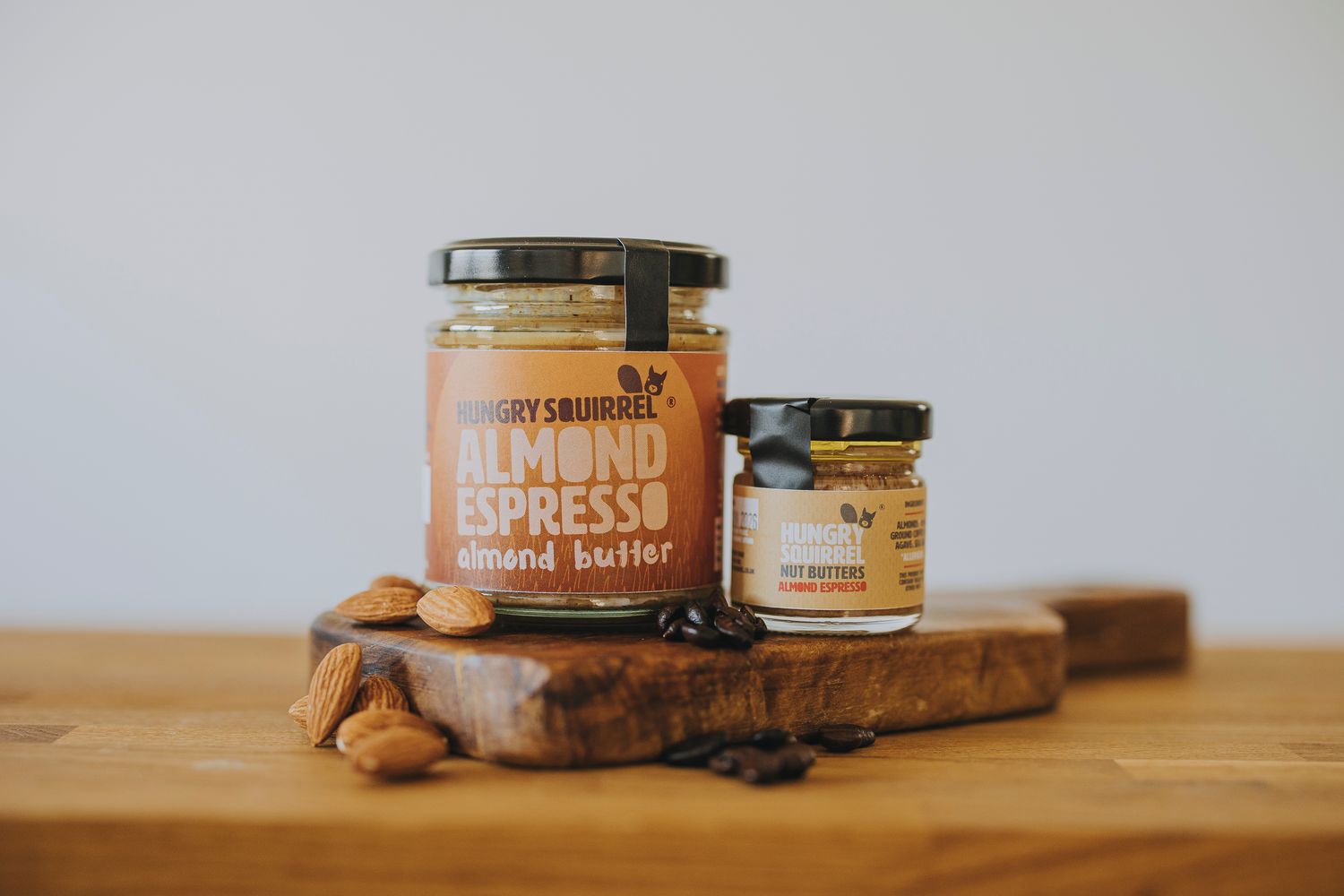 Almond Espresso Nut Butter 180g jar and 40g taster jar displayed on a wooden board with coffee beans and almonds.