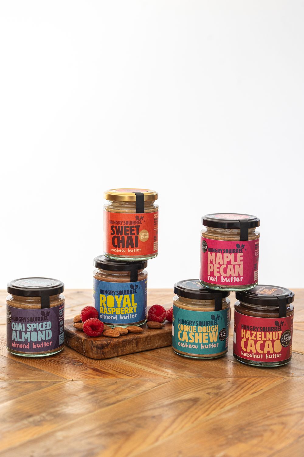 Assorted 40g nut butter taster jars in different flavours arranged in a pyramid display on a wooden surface.