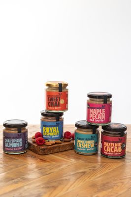 Assorted 40g nut butter taster jars in different flavours arranged in a pyramid display on a wooden surface.