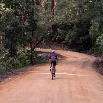 A cyclist rides away from the camera into a red clay gravel path in the bush