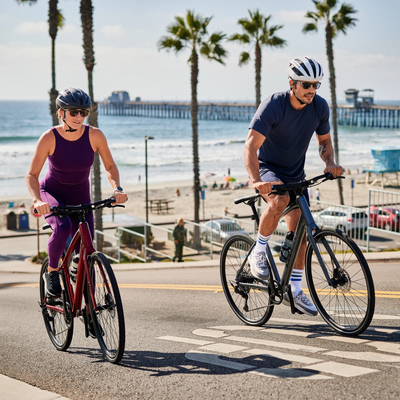 Two cyclists ride up a hill away from the palm tree-lined beach boulevard on flat bar city bikes