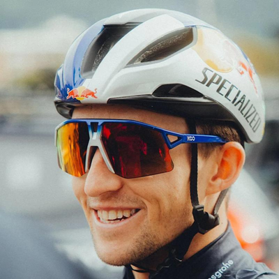 A cyclist smiles off to the left of the camera wearing a Red Bull helmet with a pair of Koo Hype sunglasses