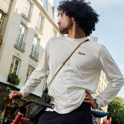 A man styles a piece of Rapha casual wear in a city street on a sunny day