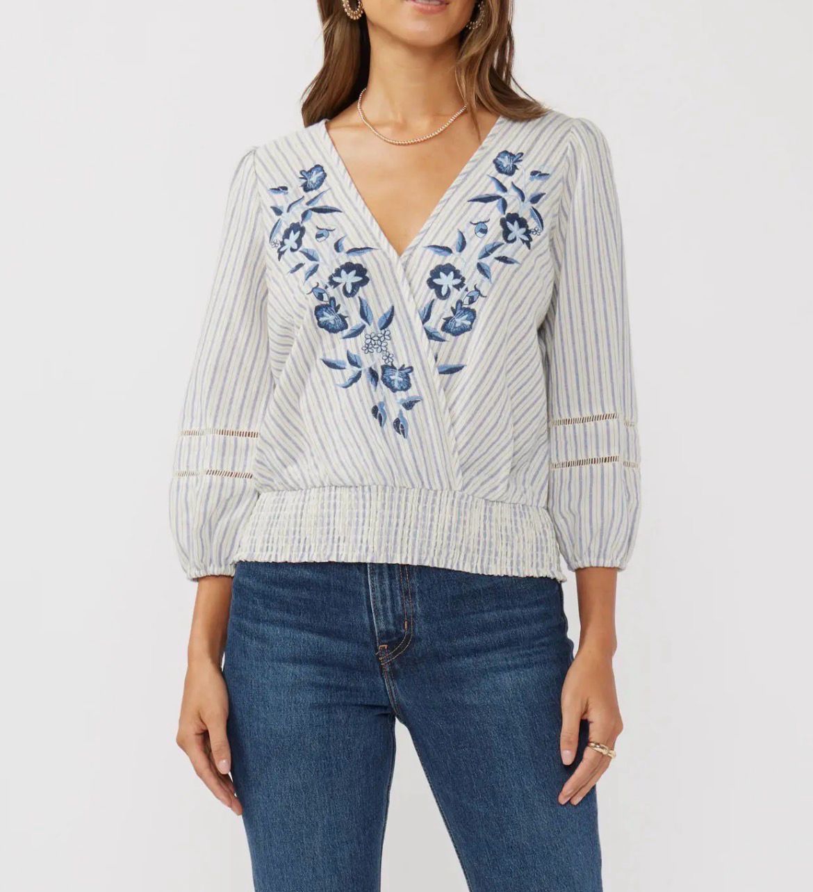 Woman wearing Lovestitch navy and natural striped surplice top with a smocked waist and floral embroidery.