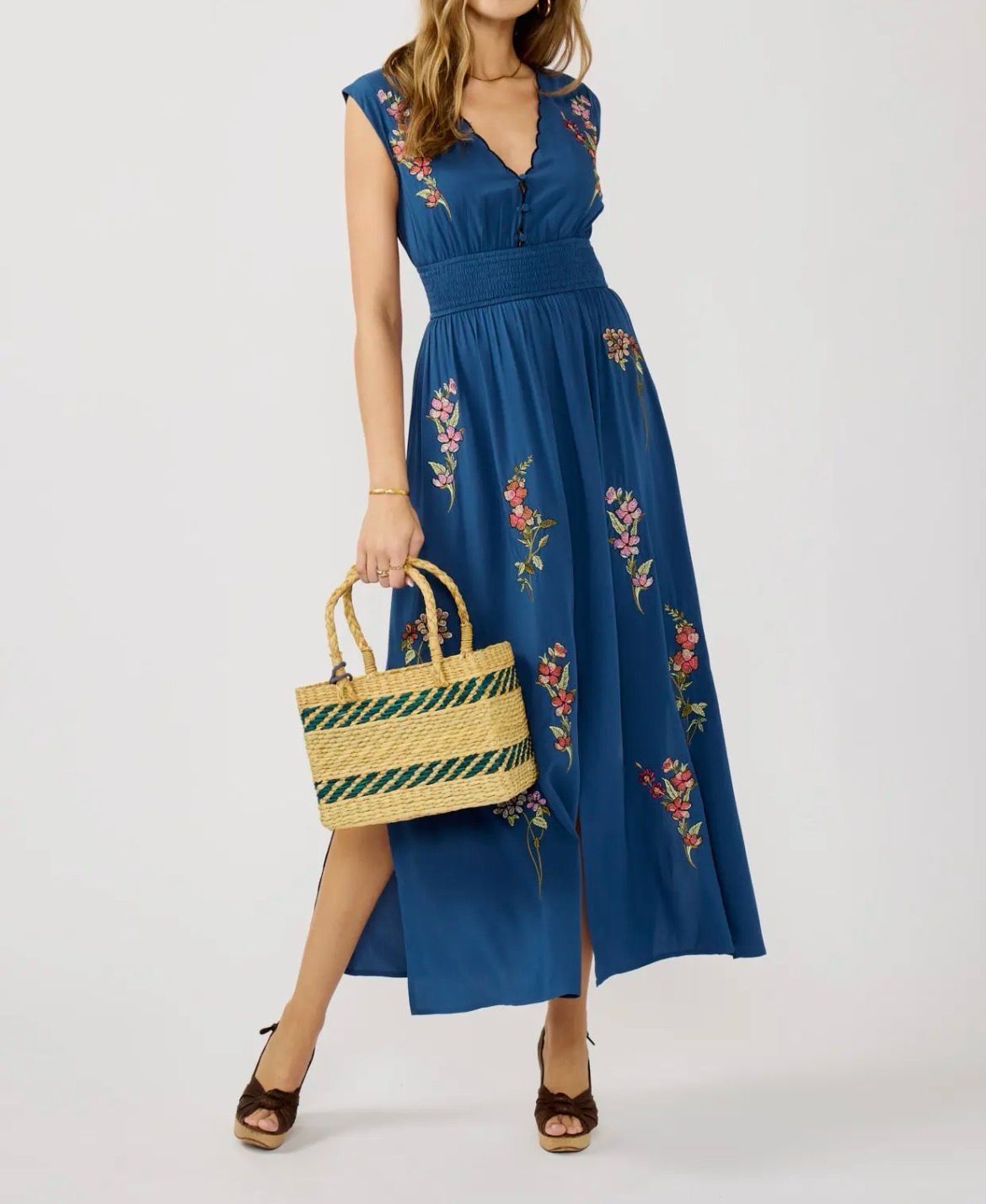 Woman in a navy blue Lovestitch maxi dress featuring colorful floral embroidery, a scalloped neckline, and a smocked waist.