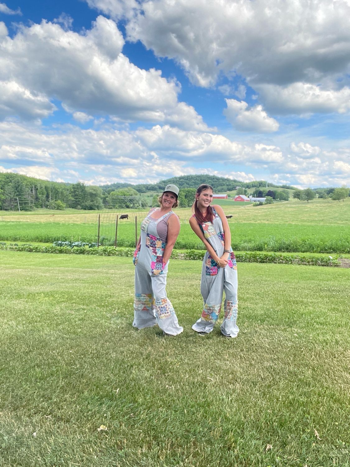 Whiskey Farmer owner and her daughter smiling in a grassy farm field, both wearing S/M gray Patchwork Boho Overalls.