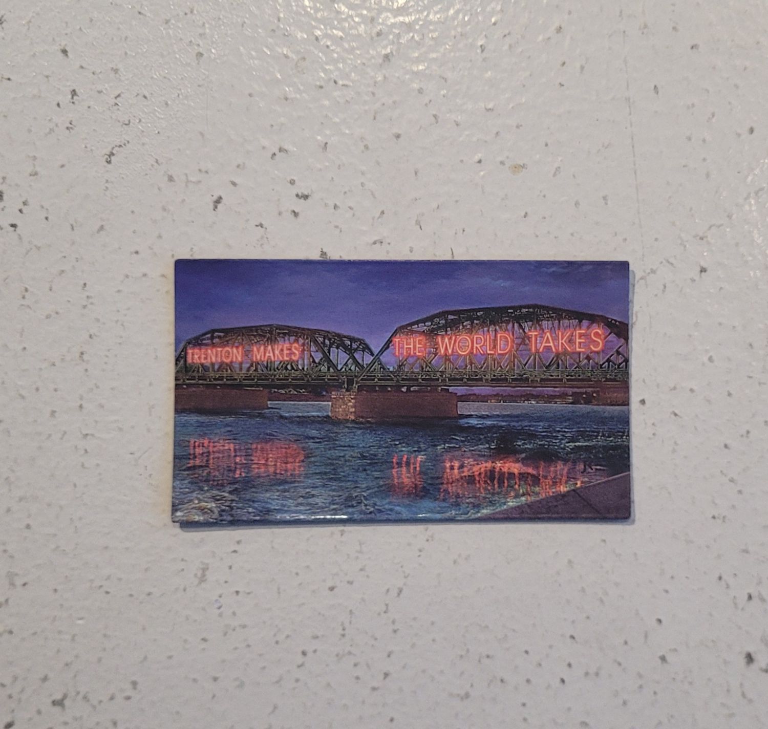 A magnet featuring the Trenton Makes, The World Takes bridge, lit up in red neon on a blue background.