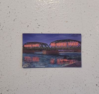 A magnet featuring the Trenton Makes, The World Takes bridge, lit up in red neon on a blue background.