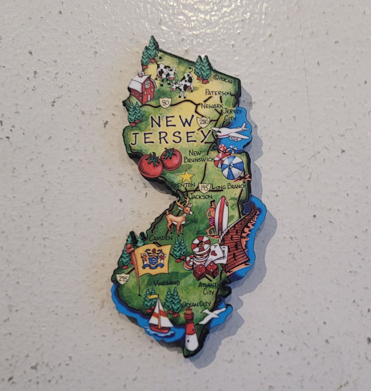 A magnet shaped like the state of New Jersey, mostly green but with icons and art across the state.