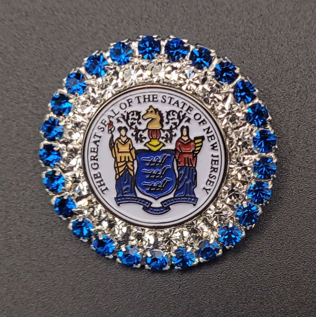 A jeweled brooch featuring the Great Seal of the State of New Jersey with blue jewels around the rim.