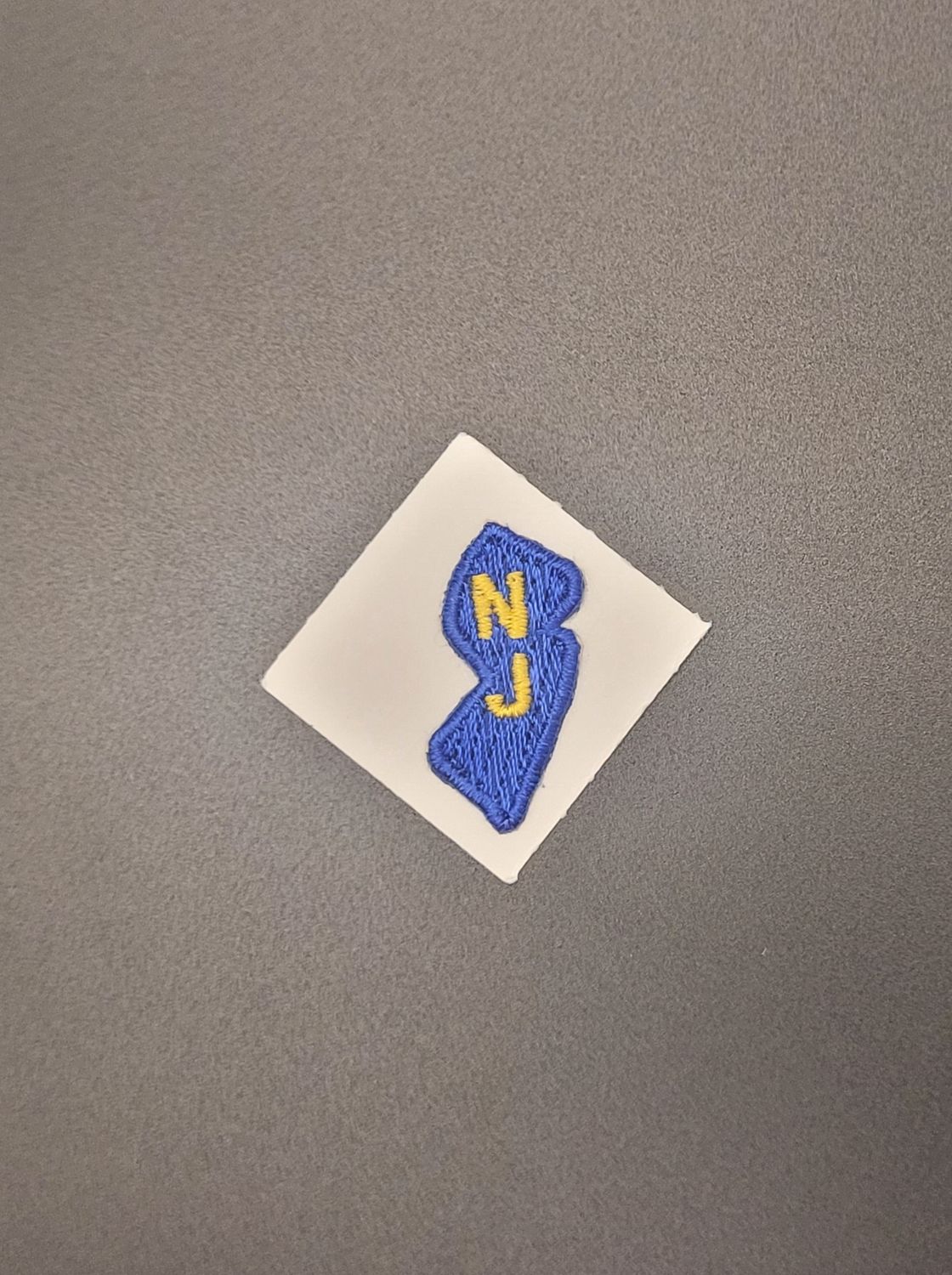 A blue patch with the letters N and J on it in the shape of New Jersey.