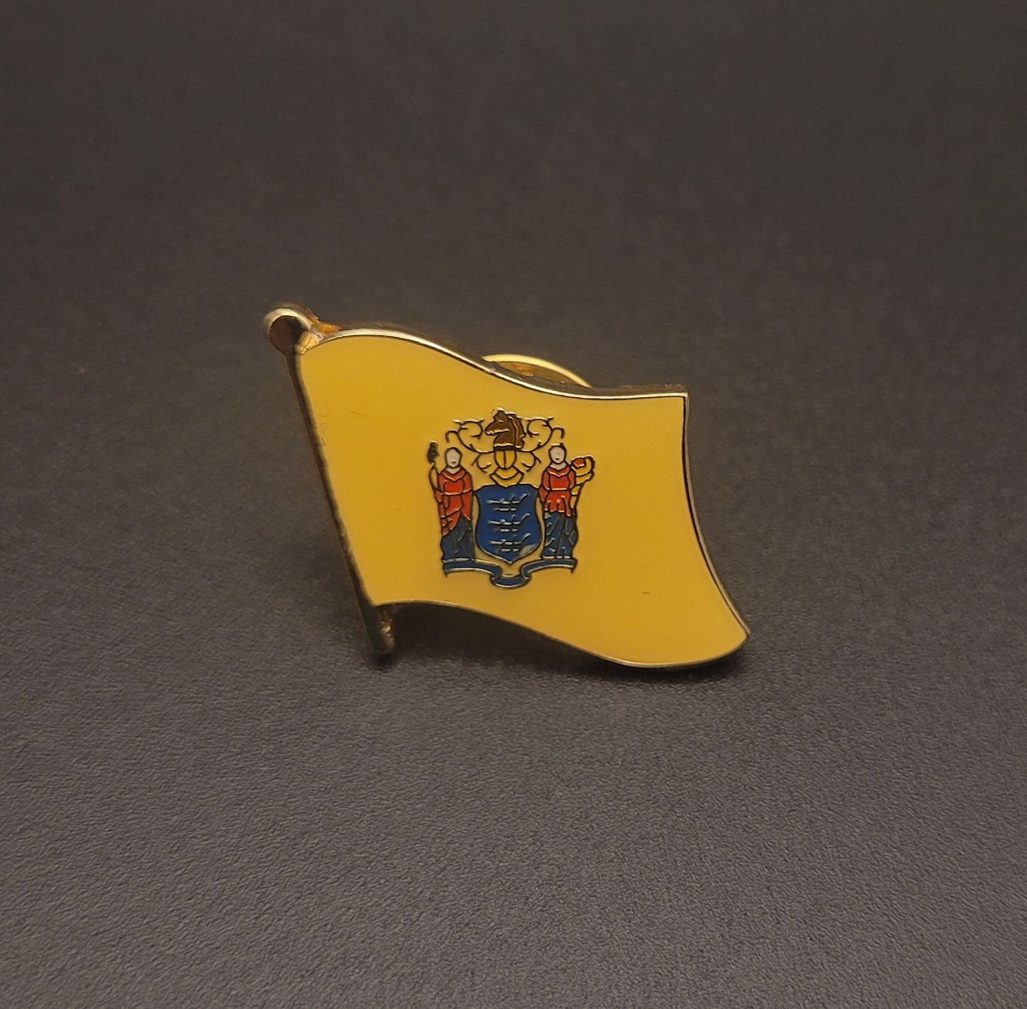 A yellow lapel pin of the flag of New Jersey with the Great Seal in the middle of it.