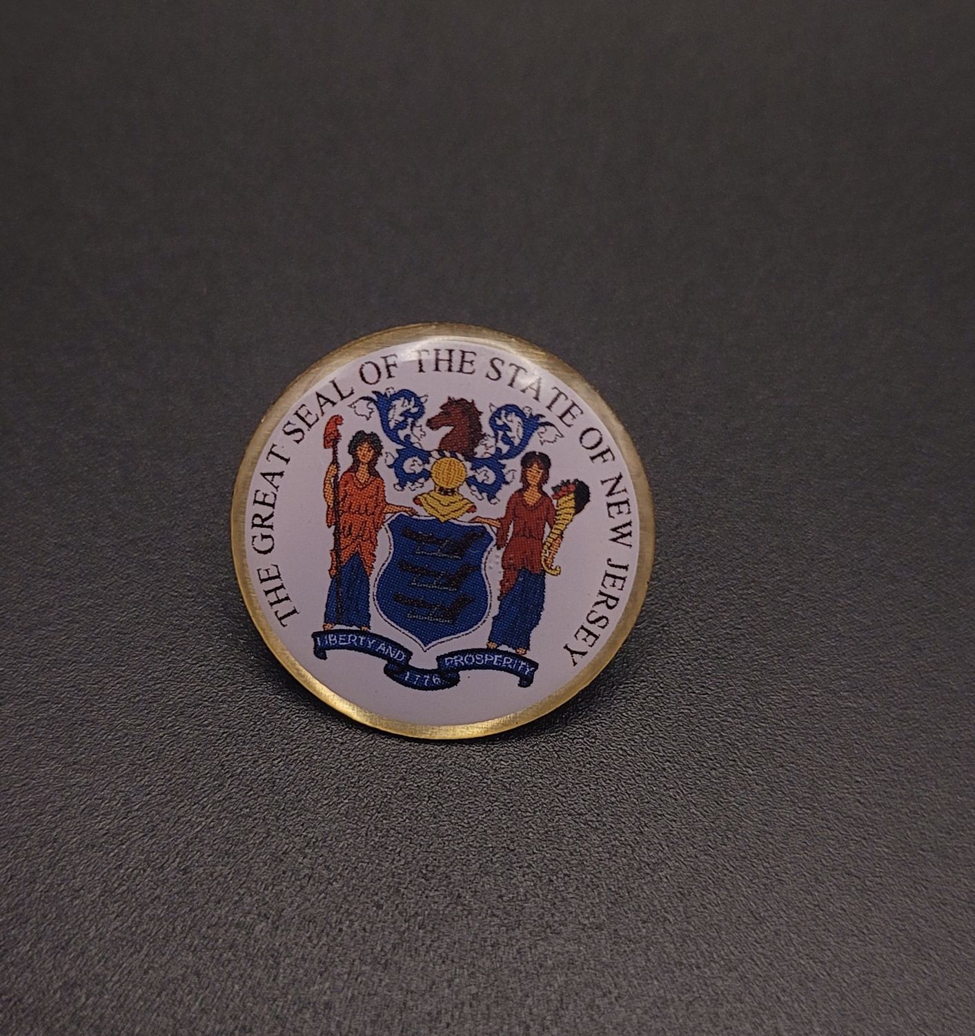 A white lapel pin featuring the words 'The Great Seal of the State of New Jersey' with the seal in the middle.