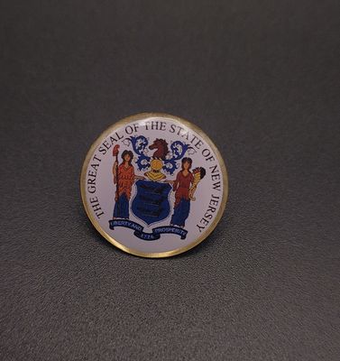 A white lapel pin featuring the words 'The Great Seal of the State of New Jersey' with the seal in the middle.