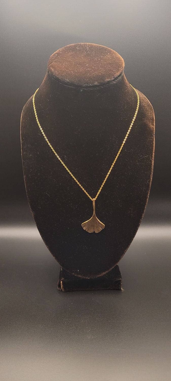 A a gold metallic ginkgo leaf pendant on a gold chain and a display stand.