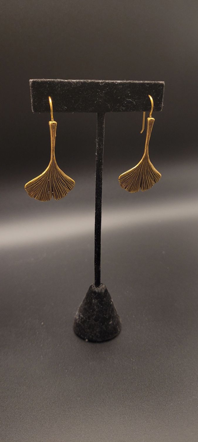 Two gold-metallic earrings featuring a ginkgo leaf on a black stand.