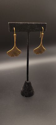 Two gold-metallic earrings featuring a ginkgo leaf on a black stand.