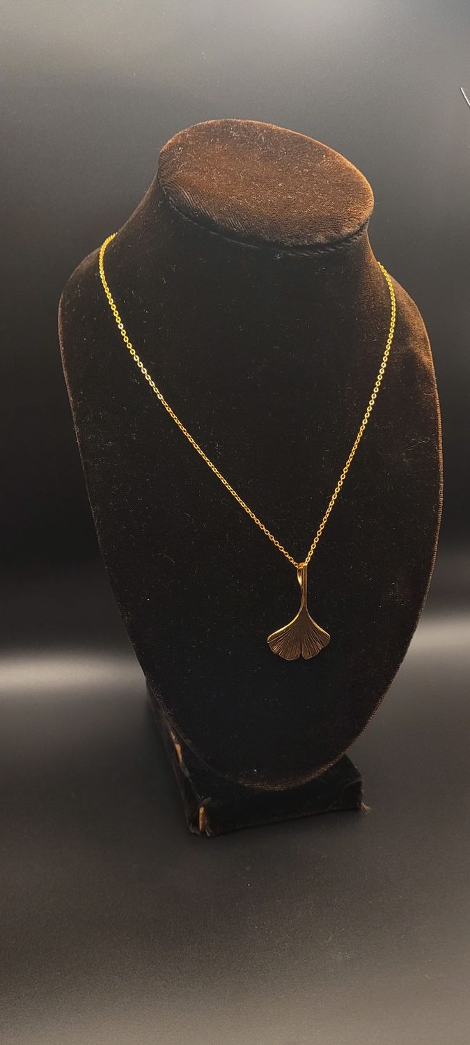 A a gold metallic ginkgo leaf pendant on a gold chain and a display stand.