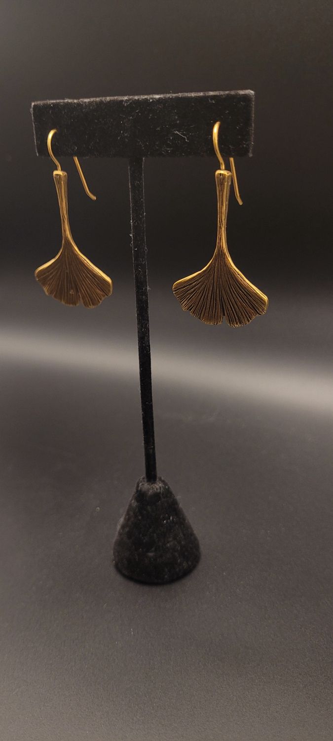 Two gold-metallic earrings featuring a ginkgo leaf on a black stand.