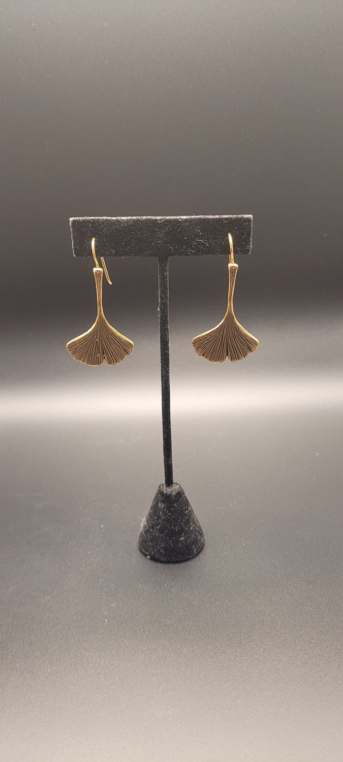 Two gold-metallic earrings featuring a ginkgo leaf on a black stand.