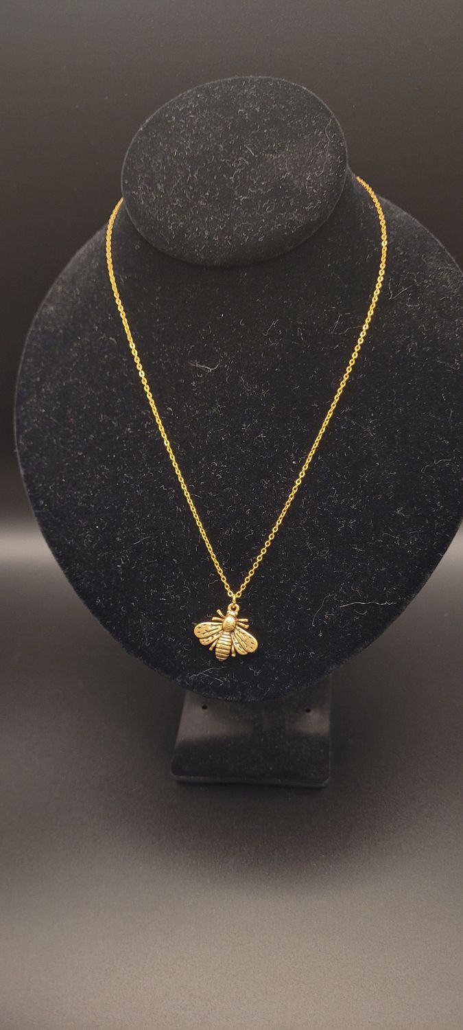 A metallic bee on a golden chain necklace on a display stand.