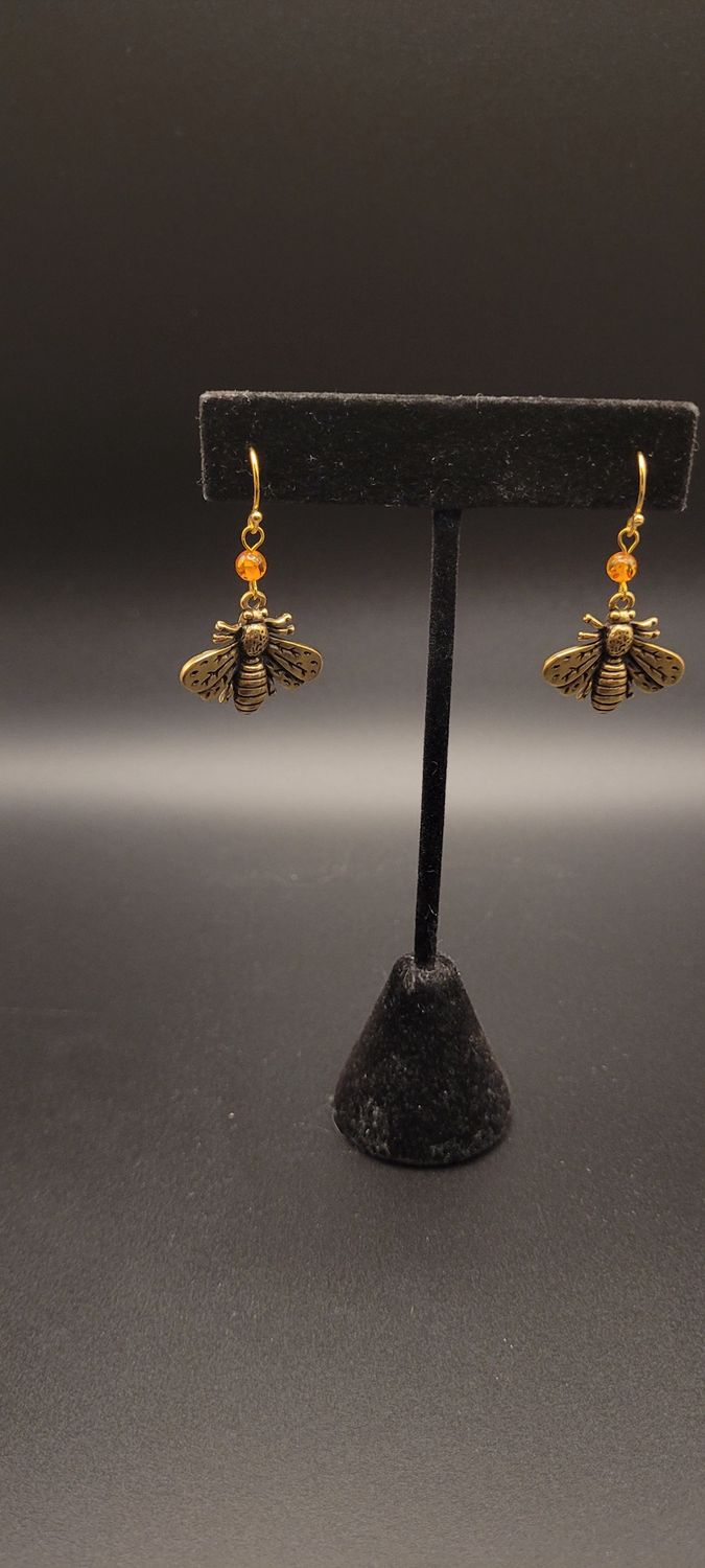 Two earrings, each with an orange amber bead and then a metallic bee beneath them.