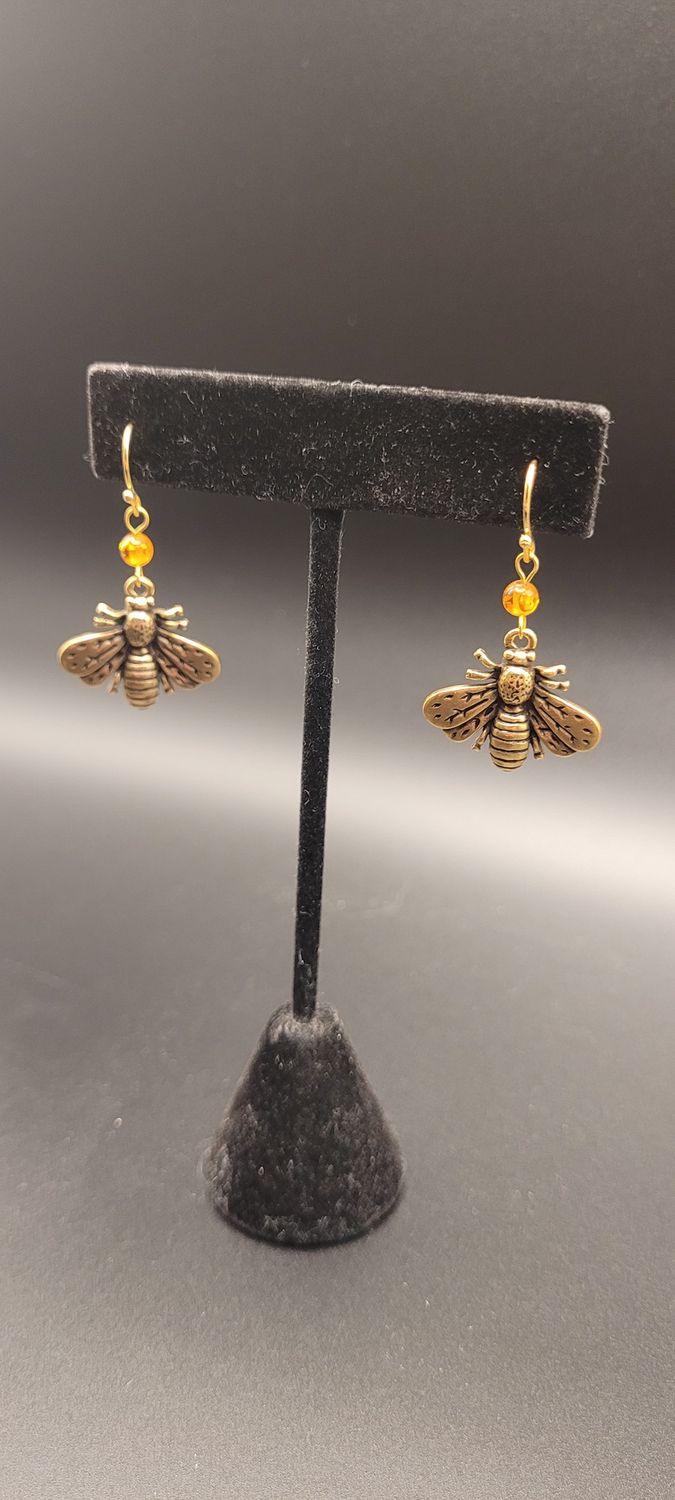 Two earrings, each with an orange amber bead and then a metallic bee beneath them.