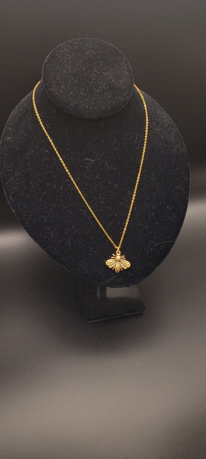 A metallic bee on a golden chain necklace on a display stand.