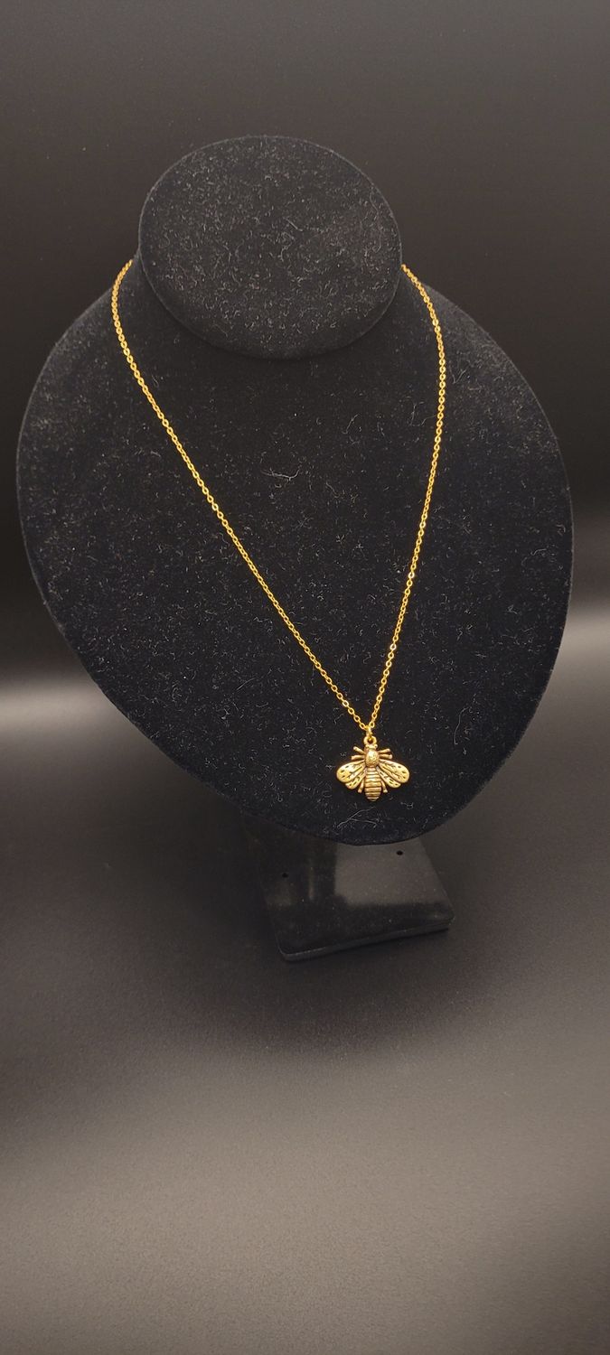 A metallic bee on a golden chain necklace on a display stand.