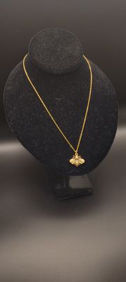 A metallic bee on a golden chain necklace on a display stand.