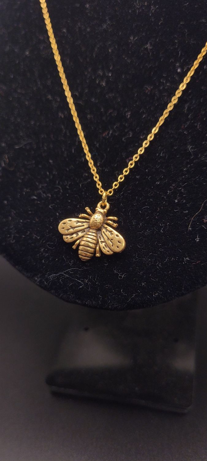 A close-up of the metallic bee on a golden chain necklace on a display stand.