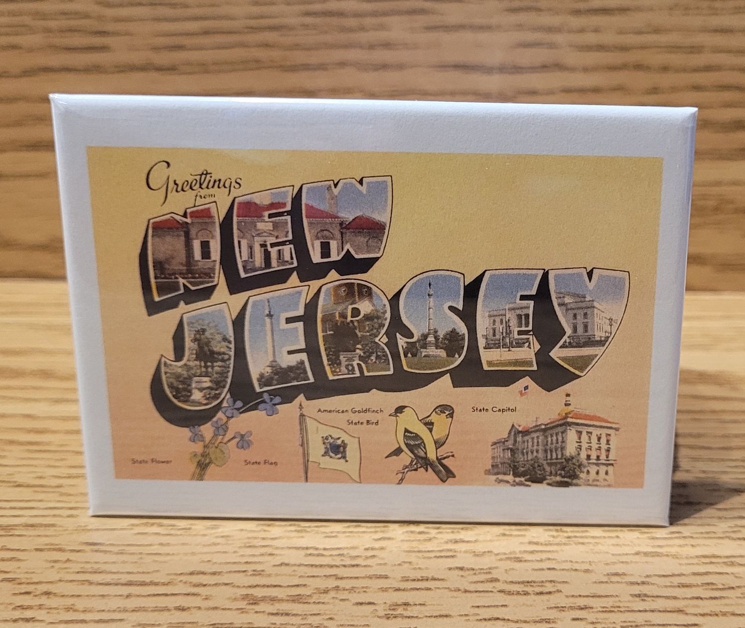 A magnet that says 'Greetings from New Jersey' in a vintage style, yellow background, featuring state icons along the bottom.