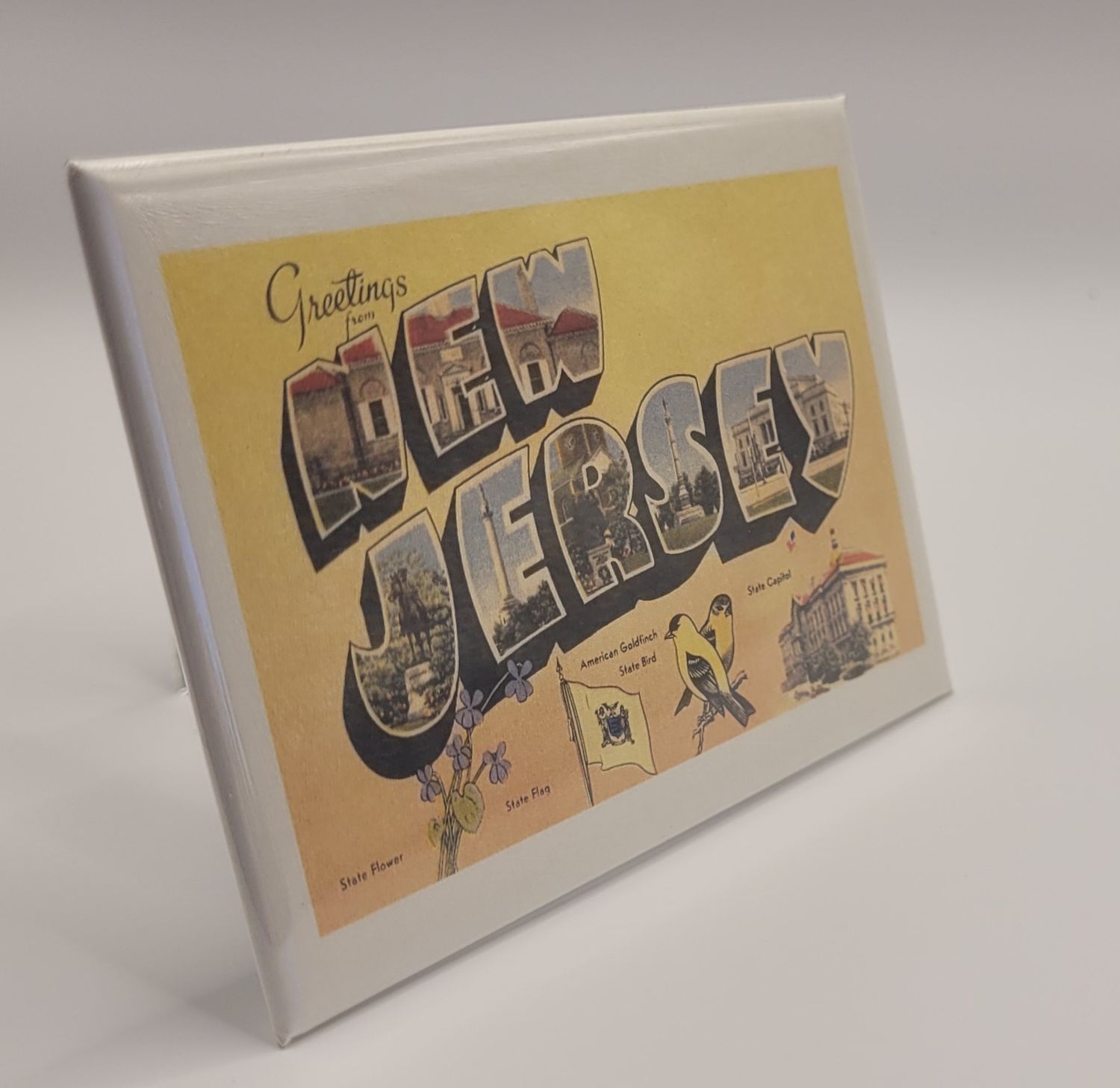 A magnet that says 'Greetings from New Jersey' in a vintage style, yellow background, featuring state icons along the bottom.