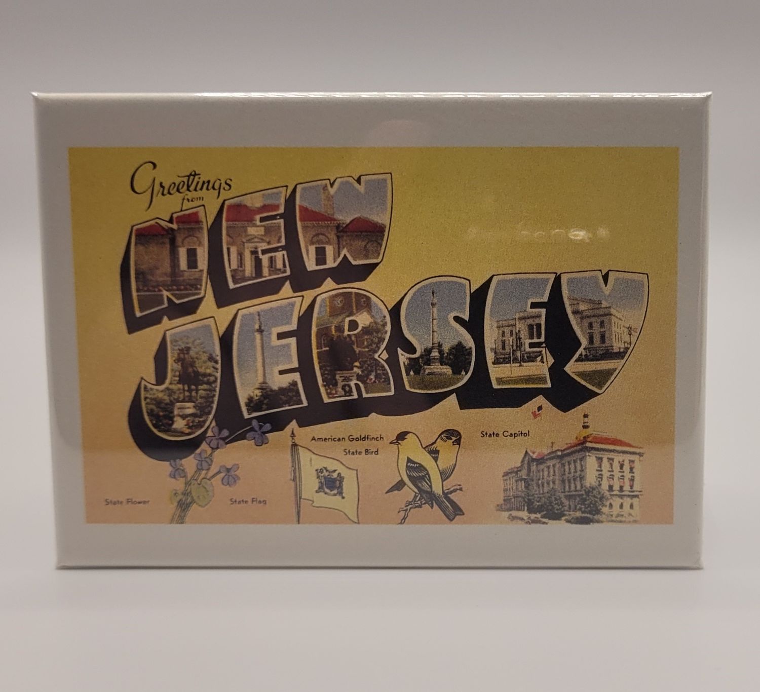A magnet that says 'Greetings from New Jersey' in a vintage style, yellow background, featuring state icons along the bottom.