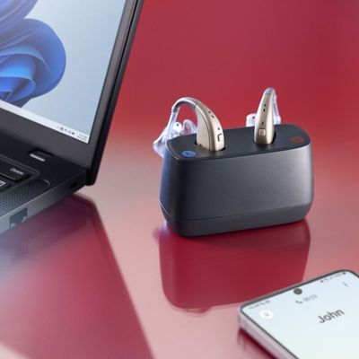 ReSound Enzo IA hearing aids in desktop charger with phone and laptop