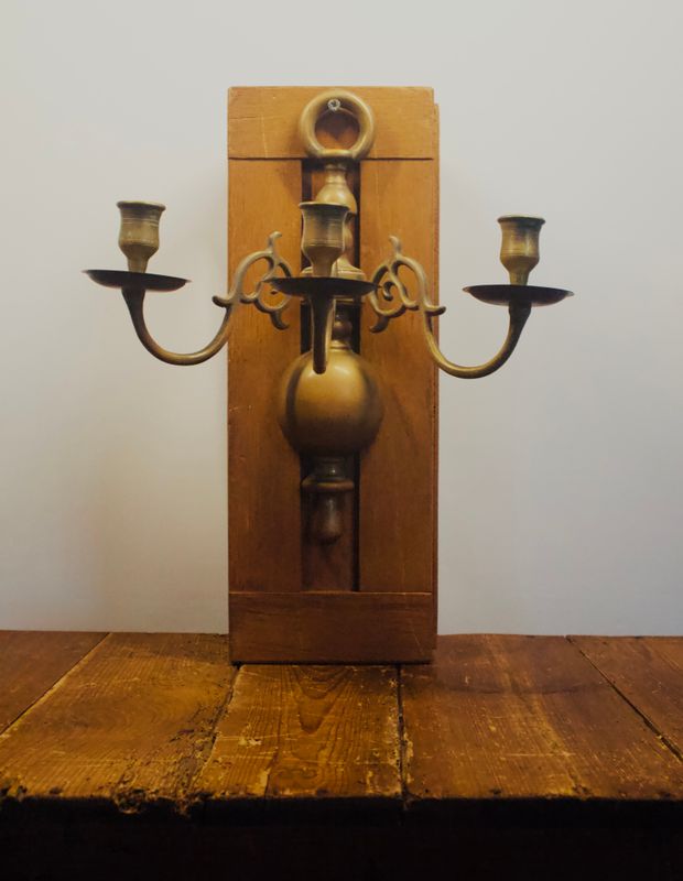 Vintage messing wandkandelaar met drie armen, bolvormige kern en sierlijke krulmotieven van de voorkant.