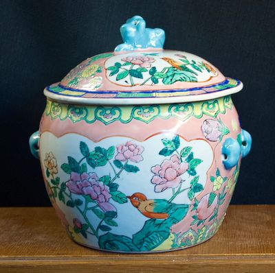 Decoratieve porseleinen pot met roze achtergrond, handbeschilderd met bloemen en vogelmotief.