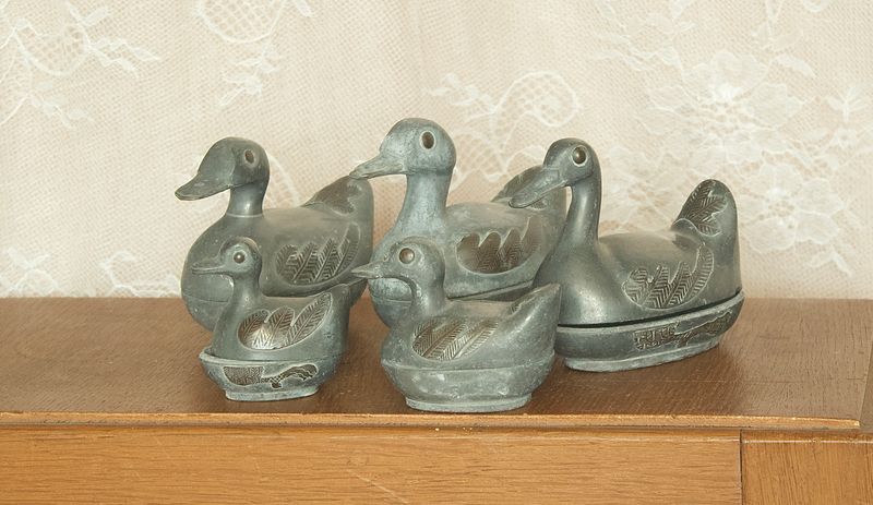 Set van 5 vintage tinnen eenden doosjes op houten dressoir met 3 grote en 2 kleine exemplaren.