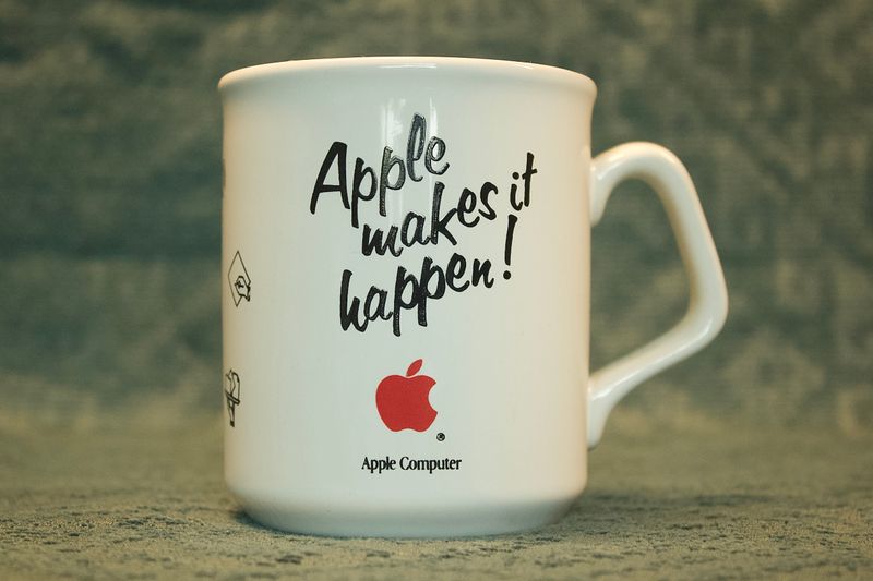 Zijaanzicht van de vintage witte Apple-mok, met de slogan 'Apple makes it happen!' in zwart schrift en een rood Apple-logo