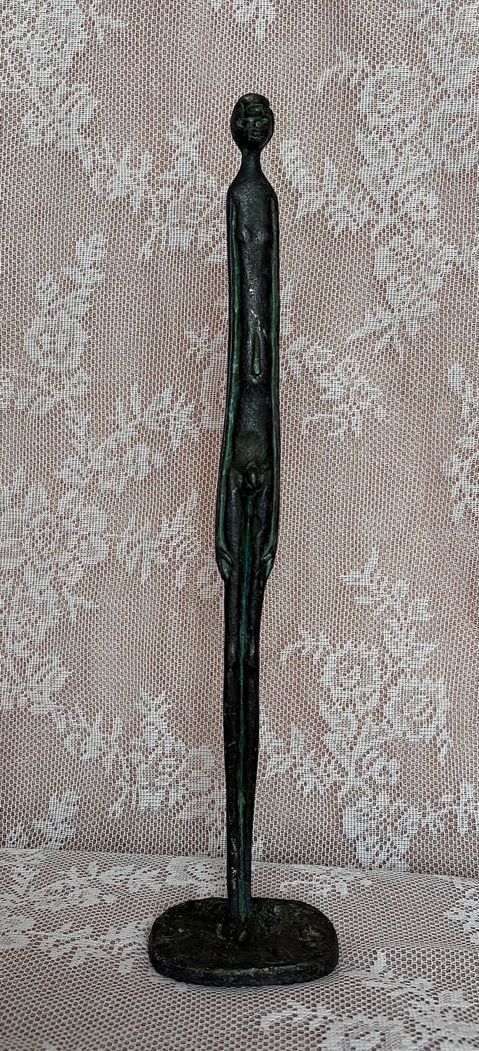 taande figuur in stijl van Giacometti, geheel vooraanzicht op de voetplaat