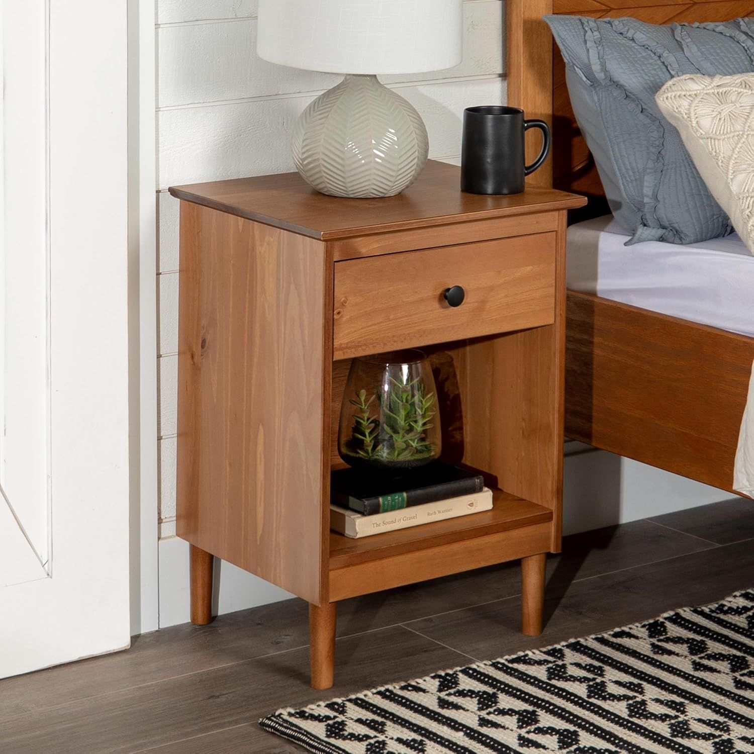 Walker Edison Traditional Wood Nightstand placed beside a bed in a cozy bedroom, styled with a lamp and decorative items.