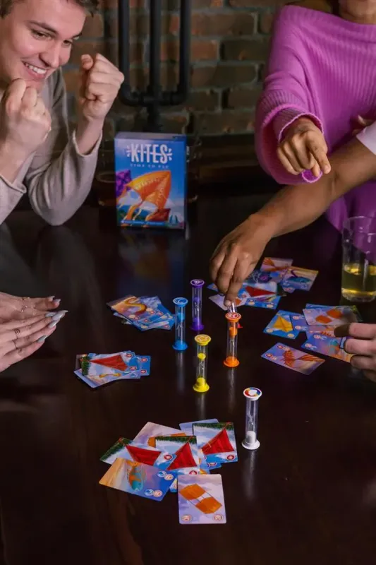 Kites board game by Floodgate Games with colorful game pieces, cards, and hourglasses on a table with four players.