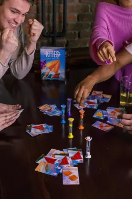 Kites board game by Floodgate Games with colorful game pieces, cards, and hourglasses on a table with four players.