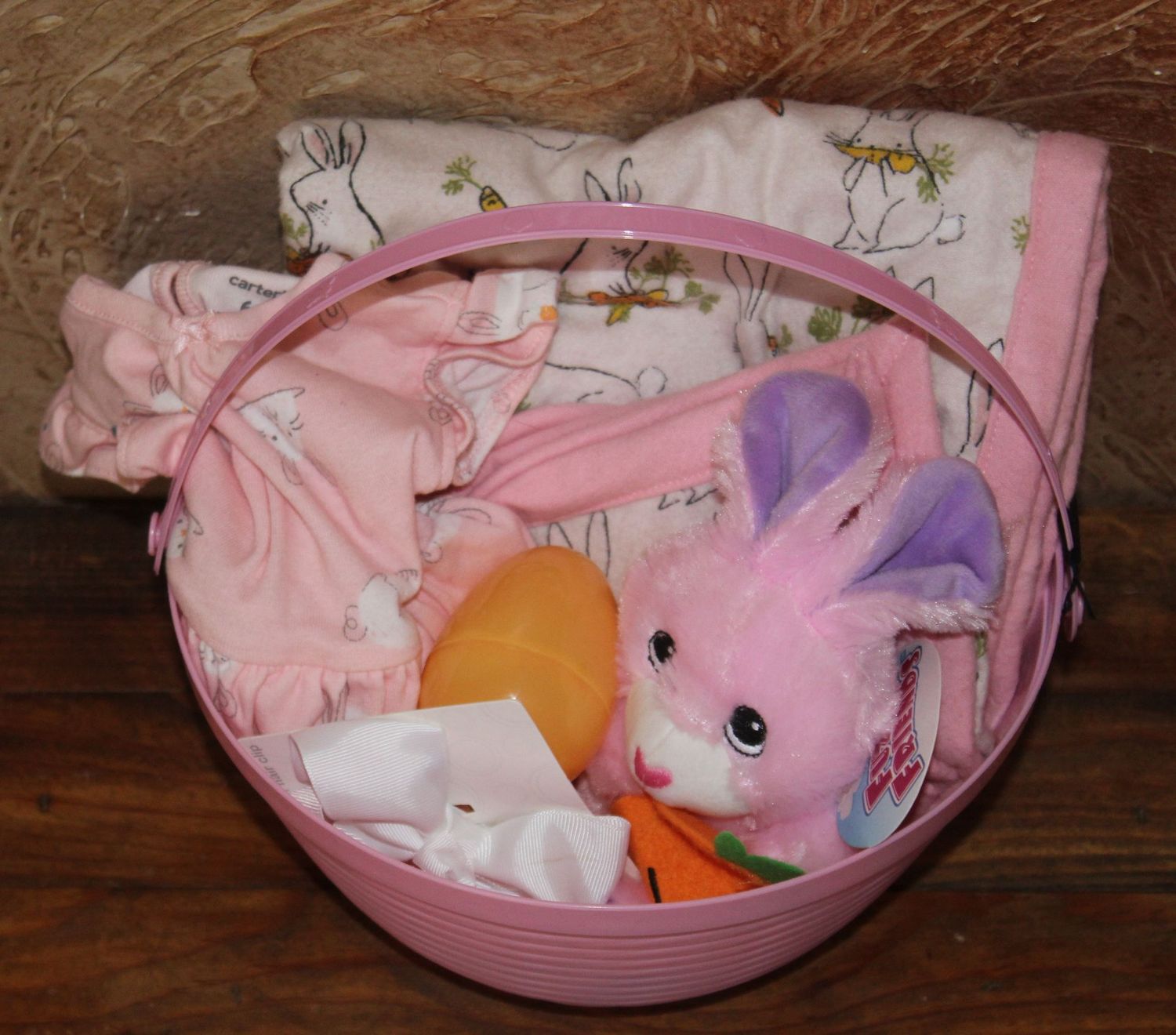 Pink baby Easter basket gift set with bunny plush, baby clothes, bow, and Easter egg