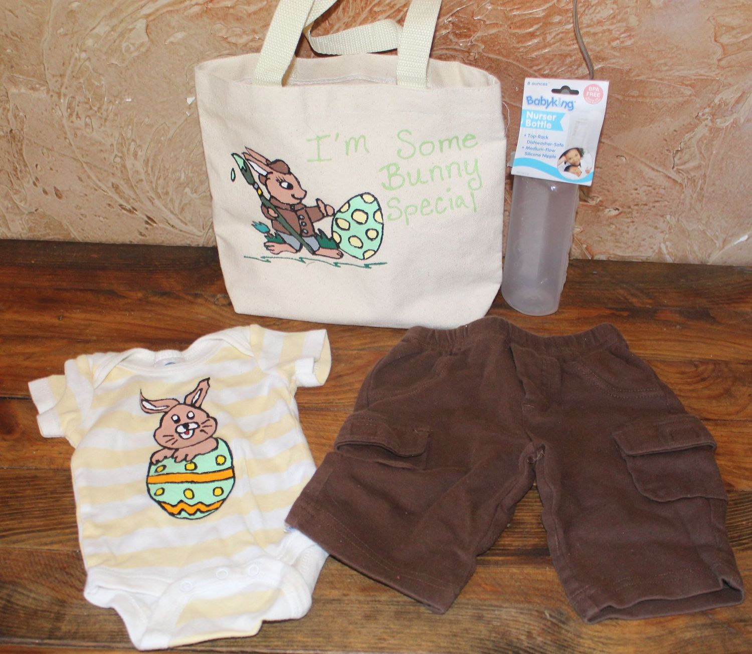 Hand-painted Easter bunny baby gift set with onesie, brown shorts, bottle, and canvas tote bag.