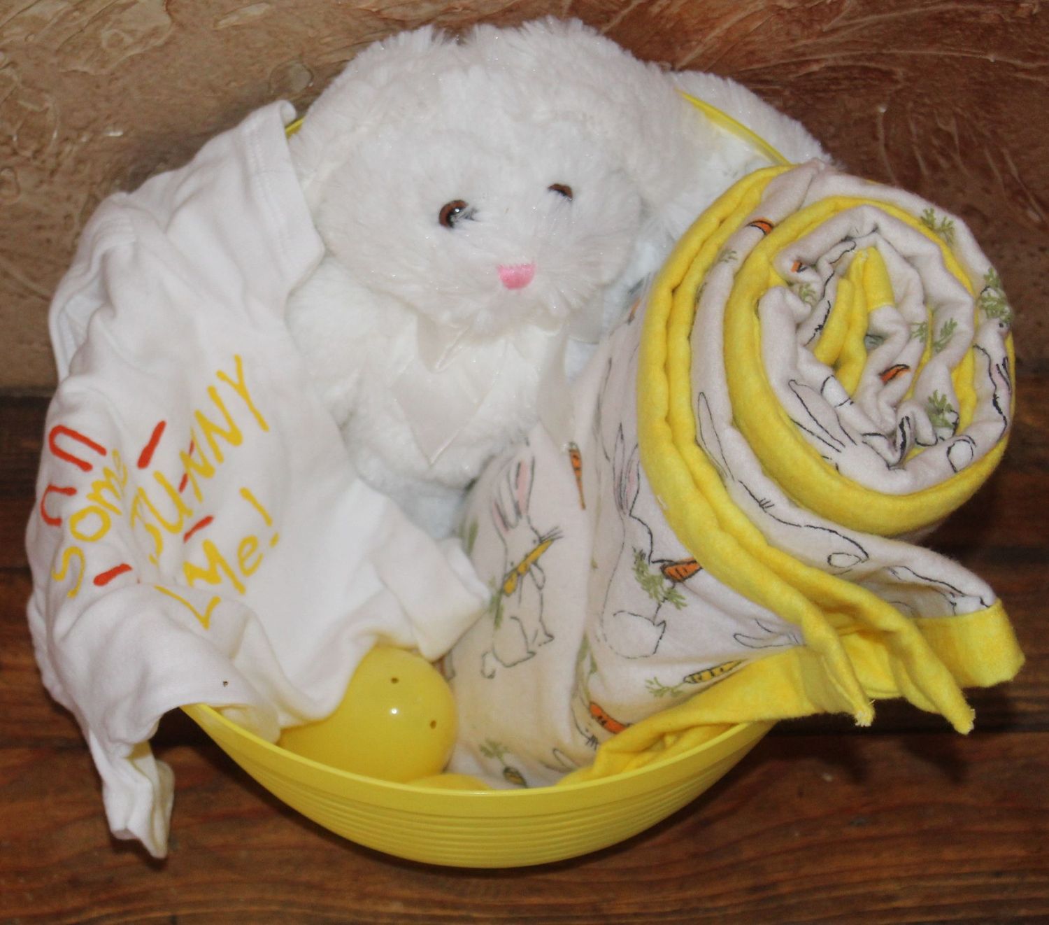 Easter baby gift basket with stuffed bunny, baby onesie, and yellow carrot themed baby blanket.