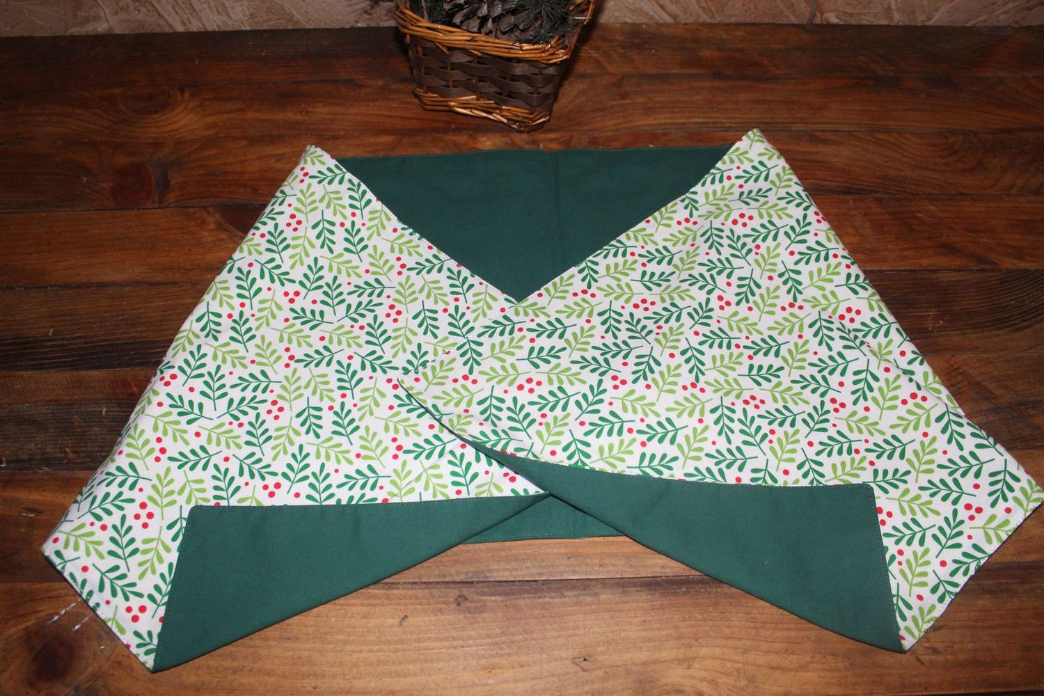 Handmade reversible Christmas table runner with holly berry print and solid green fabric displayed on wooden table