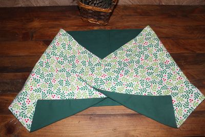 Handmade Holly Berry and Leaf Green Holiday Table Decor– Reversible Christmas Table Runner Handmade reversible Christmas table runner with holly berry print and solid green fabric displayed on wooden table