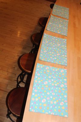 Set of Easter placemats with colorful pastel egg pattern displayed on a wooden table.