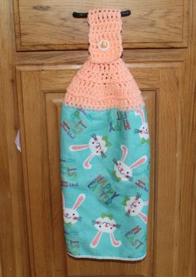 Handmade Easter kitchen towel with peach crochet topper and bunny print fabric hanging on wooden cabinet handle.